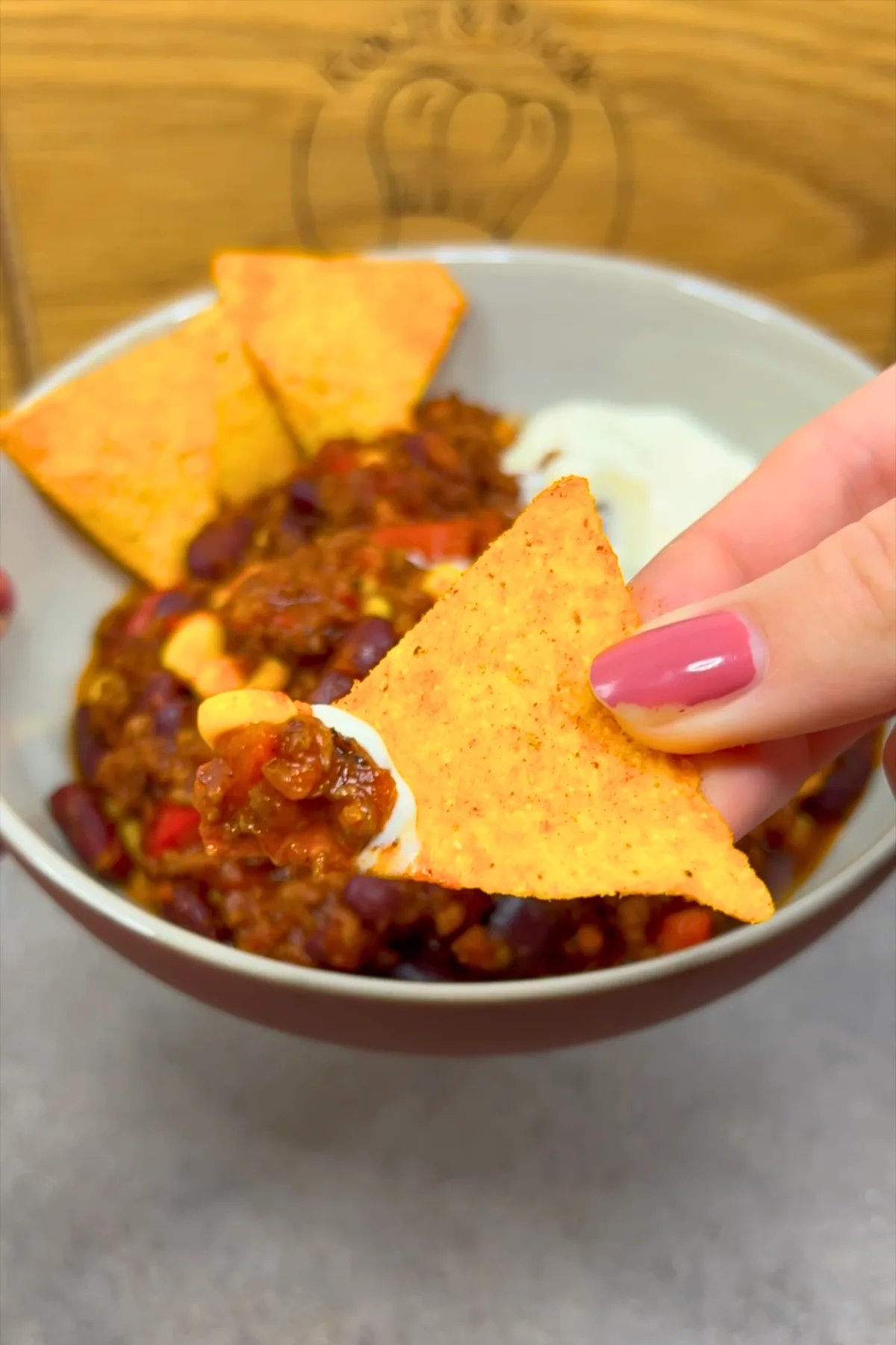 Hand greift Tortilla-Chip aus Schüssel mit Chili con Carne