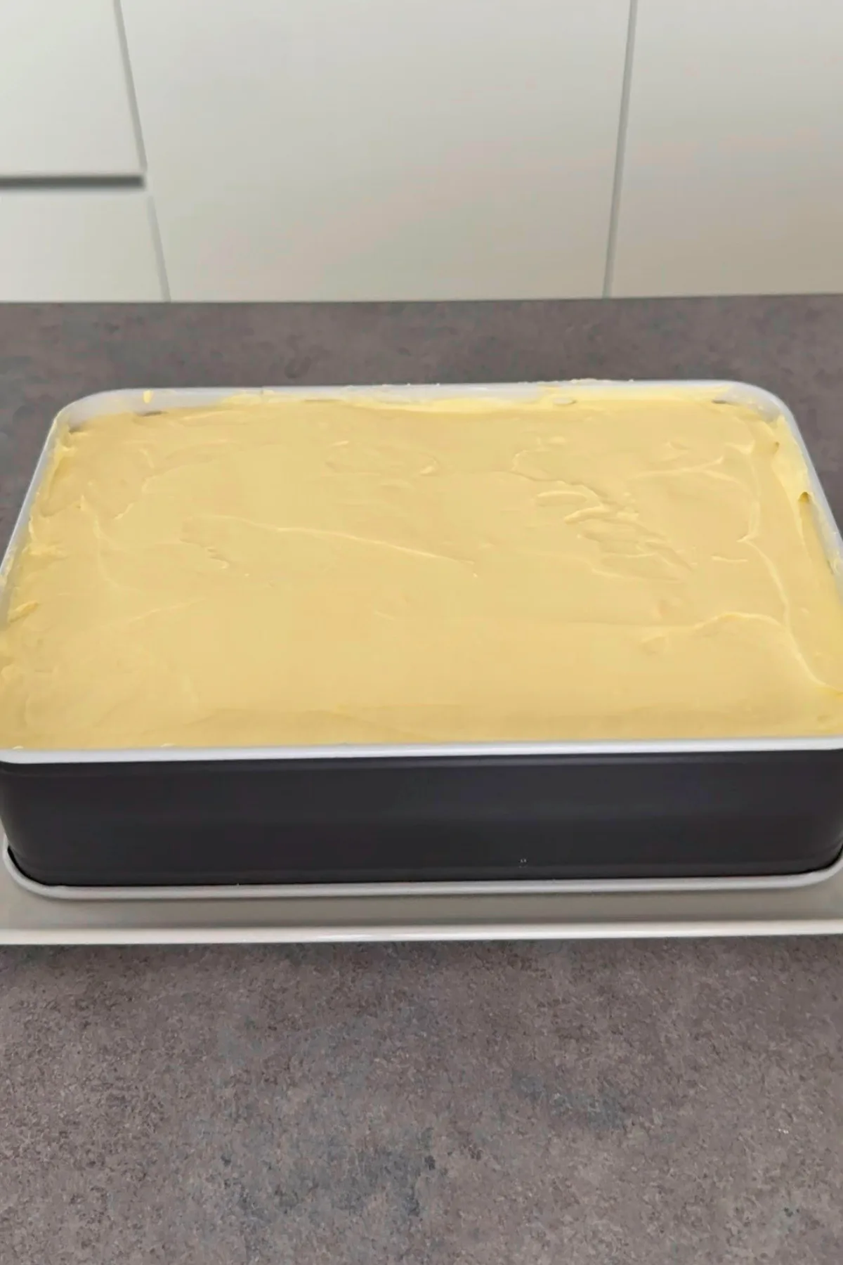 Vanille-Creme auf dem ersten Löffelbiskuit-Boden verteilt
