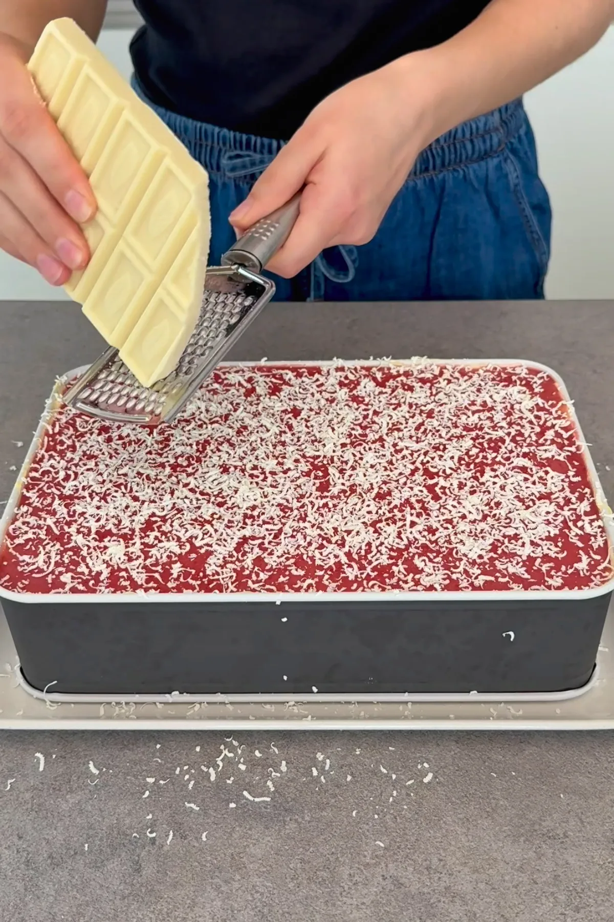 Weiße Schokolade wird über den Erdbeerspiegel des Spaghetti Eis Kuchens gerieben