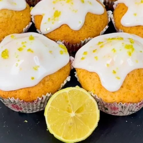 Zitronenmuffins mit weißer Glasur auf Schiefertablett mit Zitronenhälfte