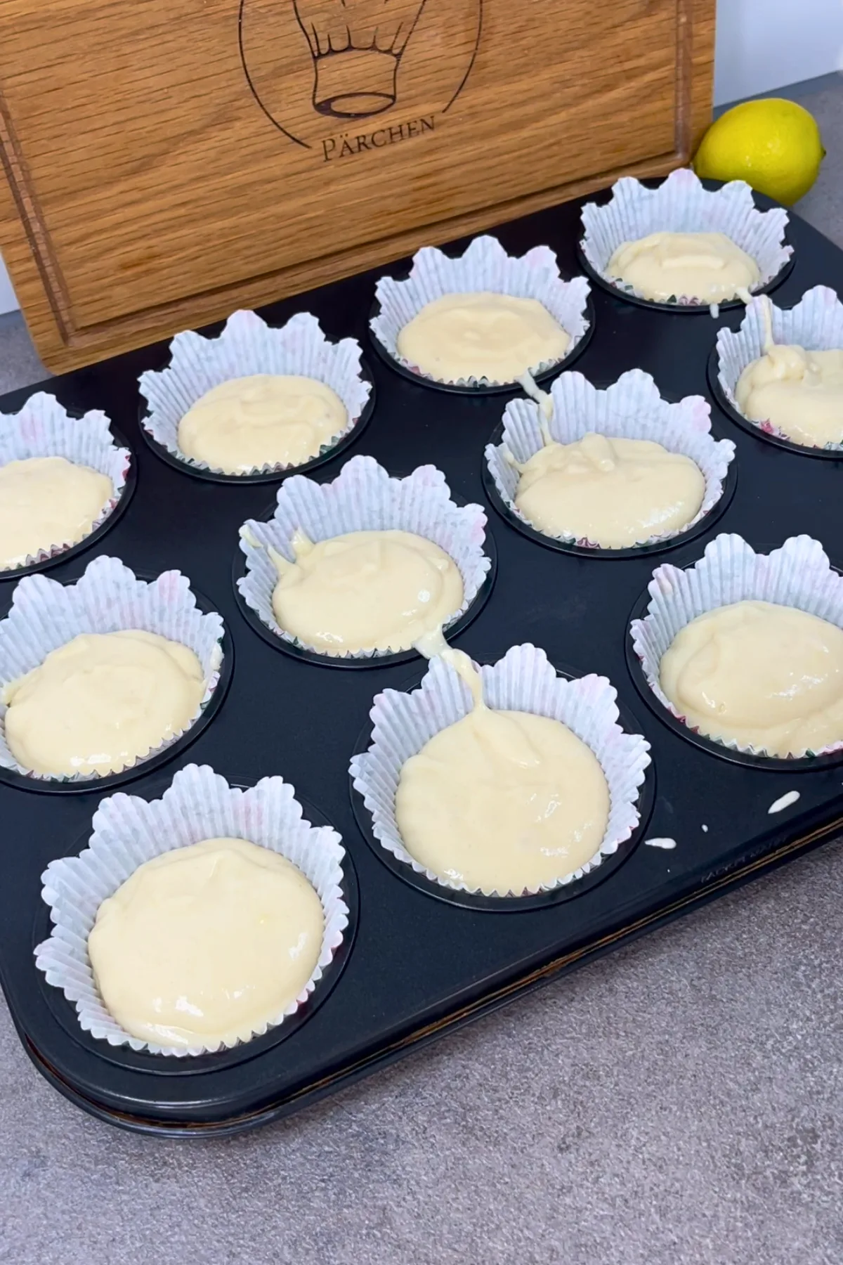Muffinblech mit 12 befüllten Papierförmchen vor dem Backen