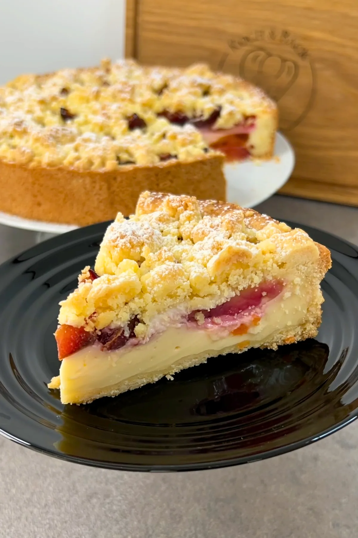 Ein Stück Zwetschgenkuchen mit Puddingschicht auf schwarzem Teller