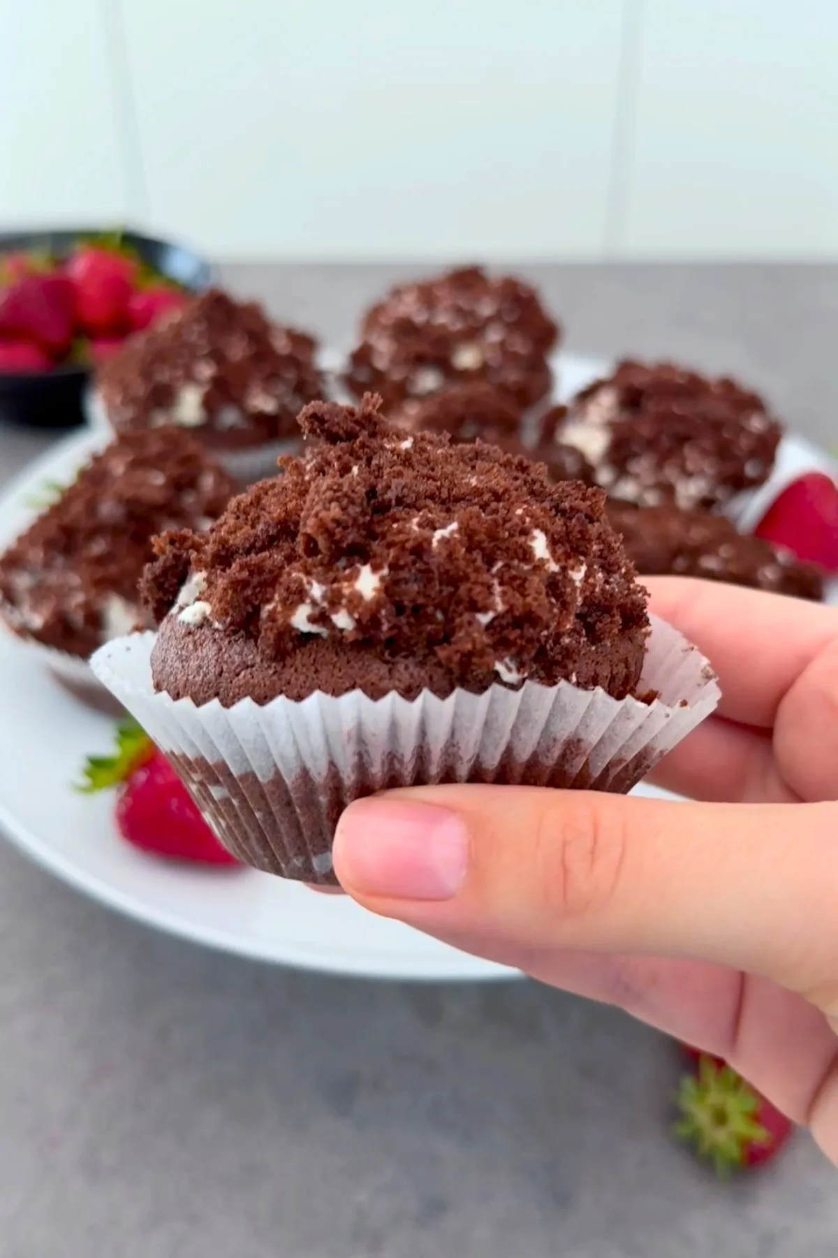Hand hält einen fertigen Maulwurfmuffin mit Schokoladenhügel hoch