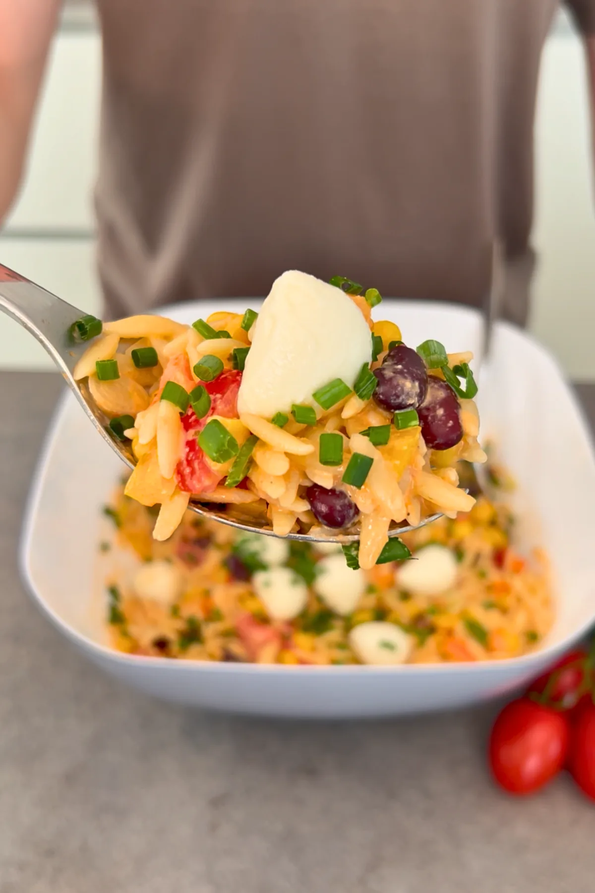 Orzo Nudelsalat in weißer Schüssel mit Löffel und frischen Tomaten