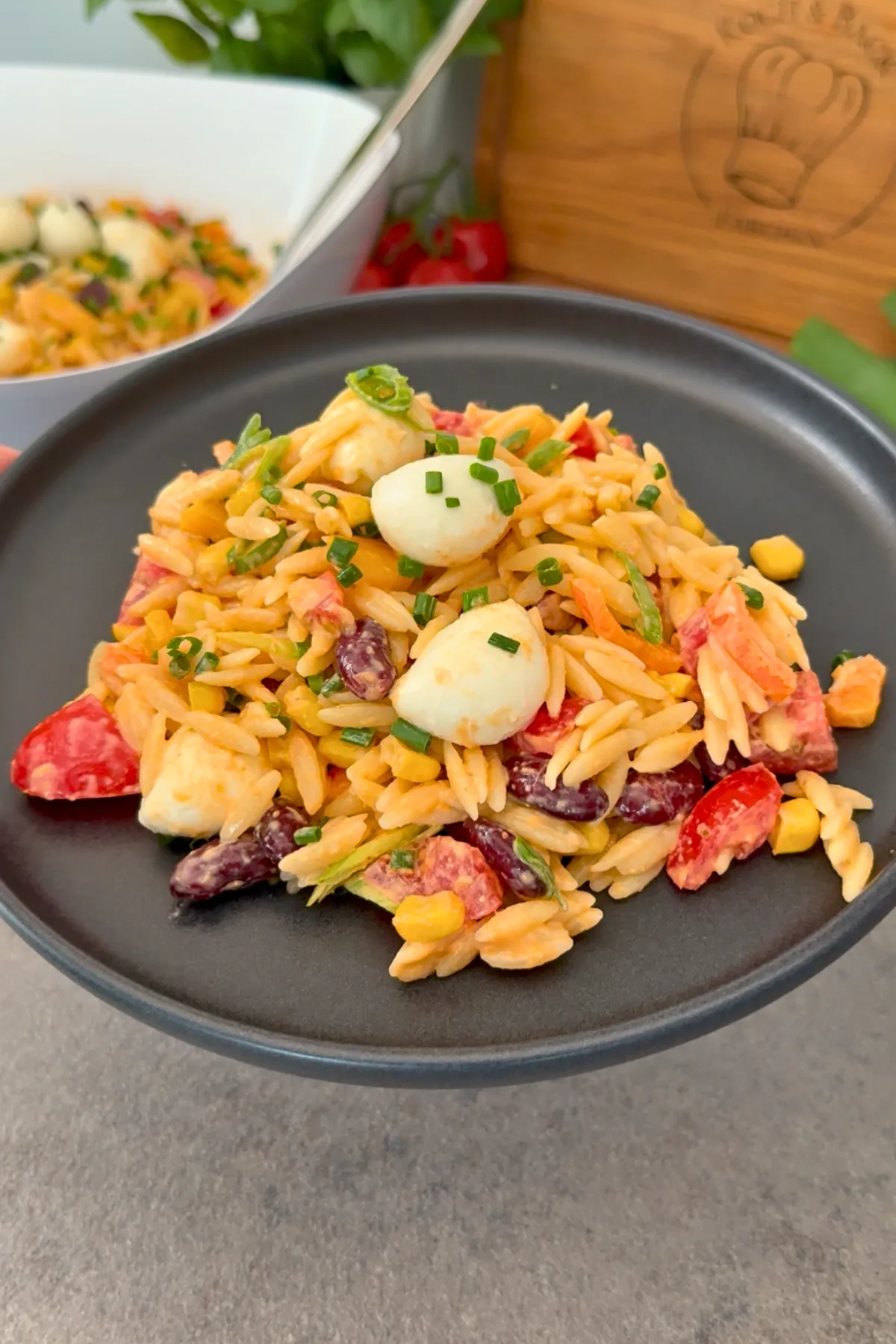 Orzo Nudelsalat auf schwarzem Teller angerichtet mit Branding-Brett