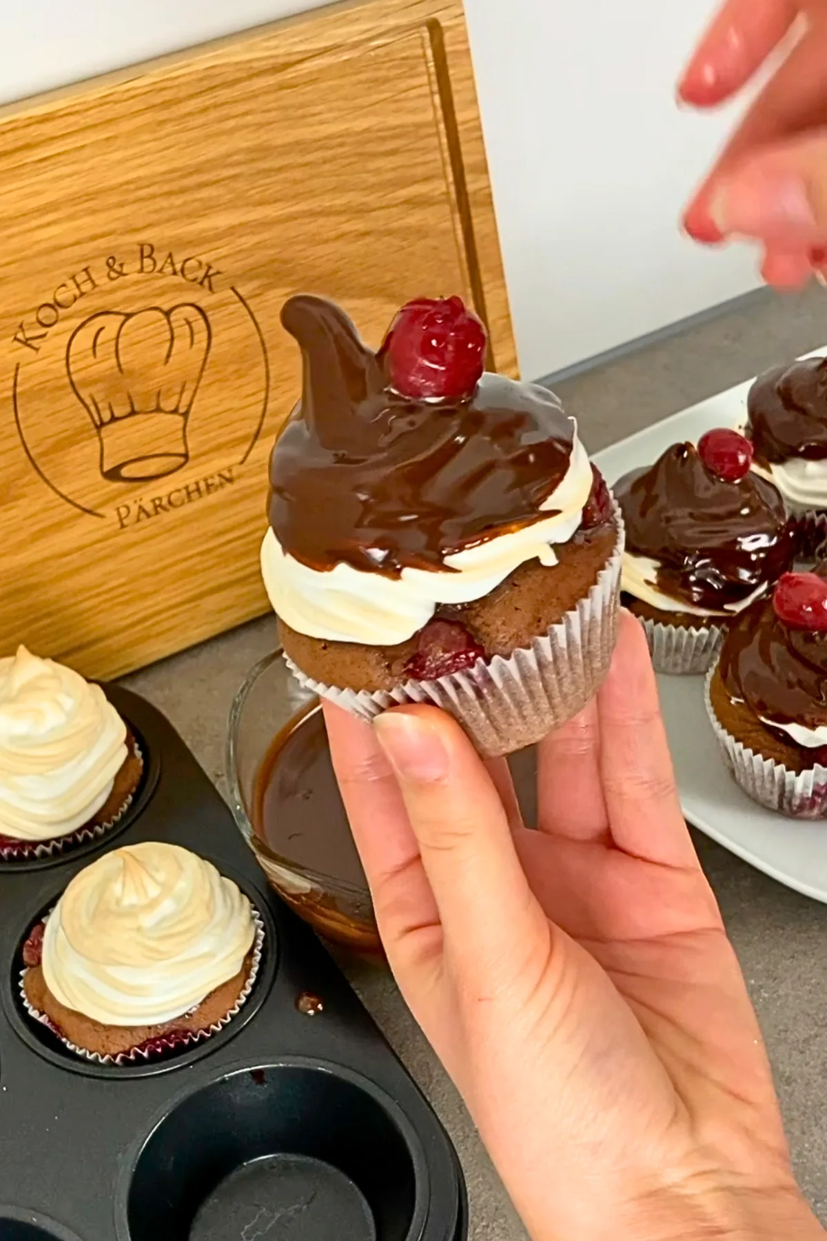 Hand hält Schwarzwälder Kirsch Muffin mit Schokoladenguss und Kirsche