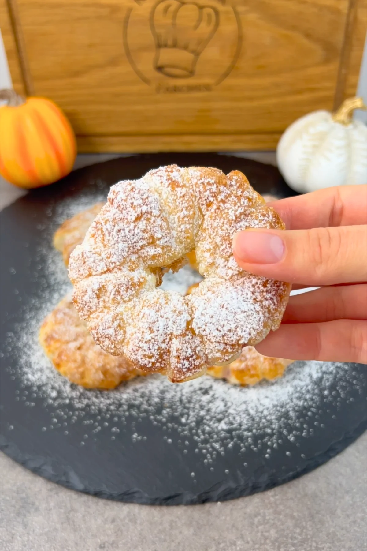 Einzelner Apfel-Donut im Blätterteigmantel wird über der Schieferplatte in der Hand gehalten