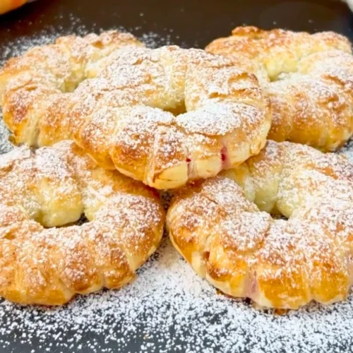Mehrere fertig gebackene Apfel-Donuts aus Blätterteig mit Puderzucker auf einer Schieferplatte