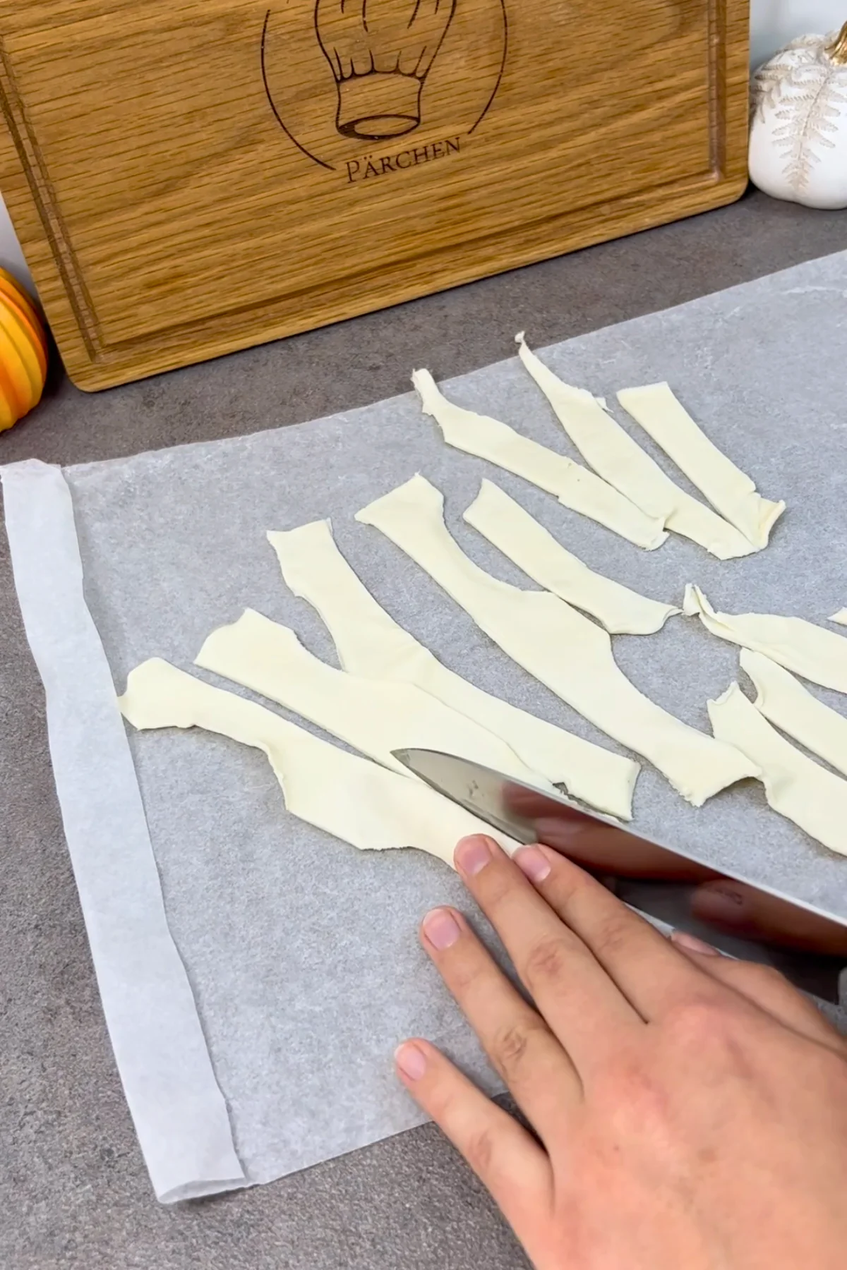 Ausgerollter Blätterteig wird auf dem Backpapier mit dem Messer in schmale Streifen geschnitten