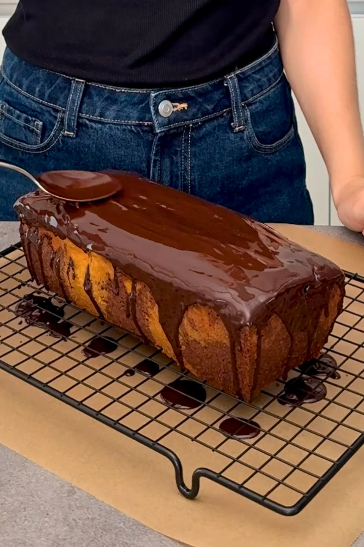 Dunkle Kuchenglasur wird mit dem Löffel auf dem abgekühlten Kuchen verstrichen
