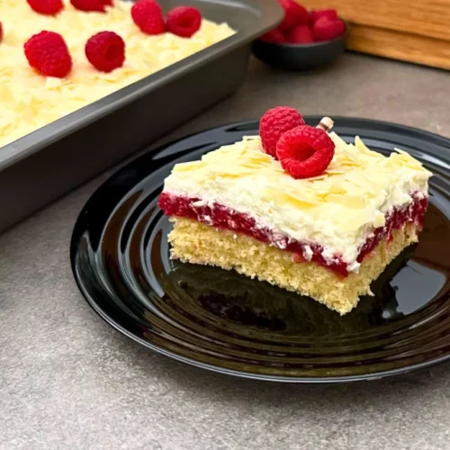 Angeschnittener Frau Holle Kuchen auf schwarzem Teller – sichtbare Schichten aus Orangenbiskuit, Himbeerfüllung und Sahnecreme