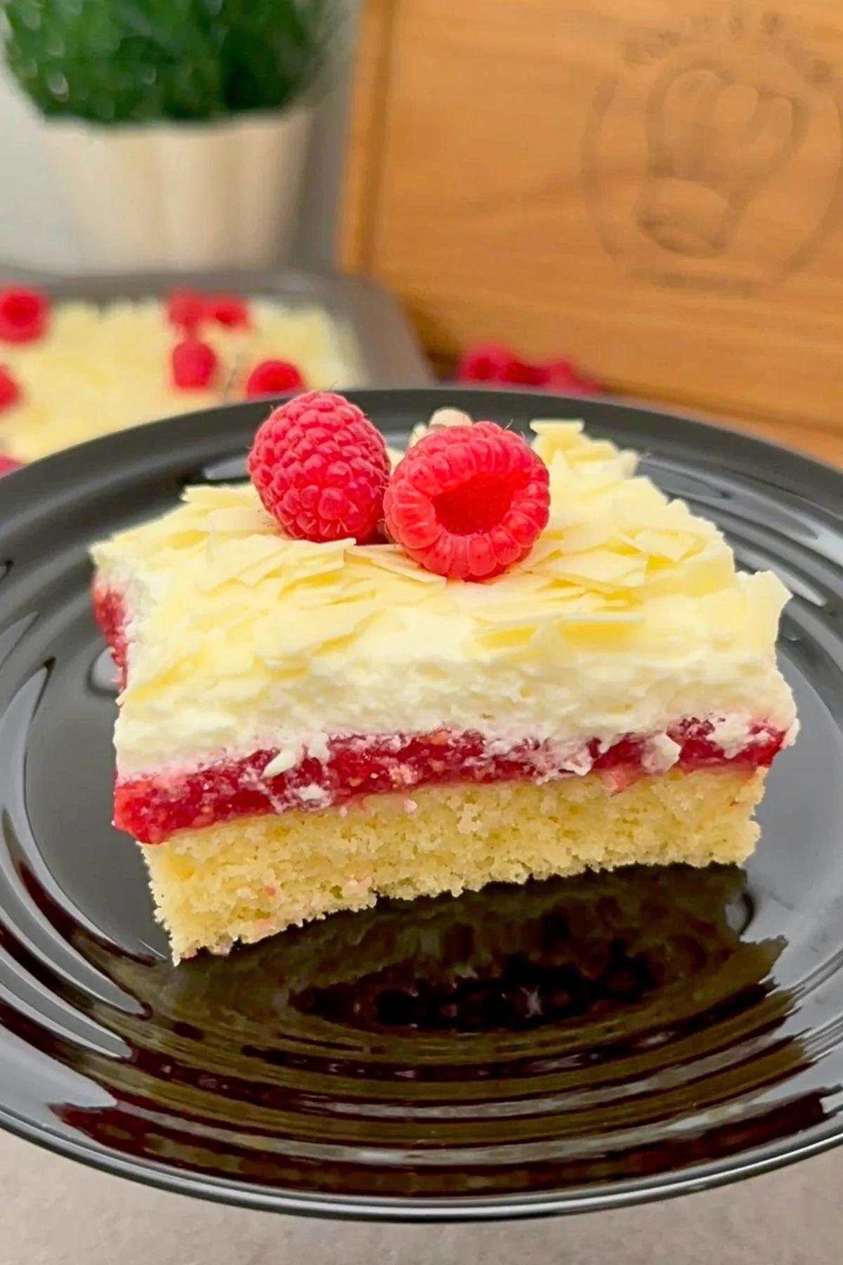 Einzelnes Stück Frau Holle Kuchen mit Himbeeren und weißer Raspelschokolade auf schwarzem Teller