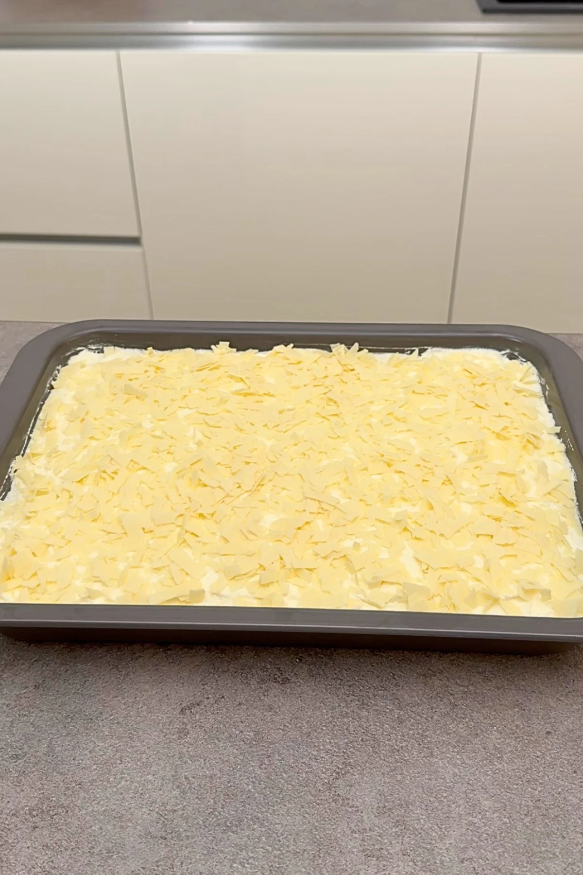 Fertig bestrichener Frau Holle Kuchen im Backblech komplett mit weißer Raspelschokolade bedeckt