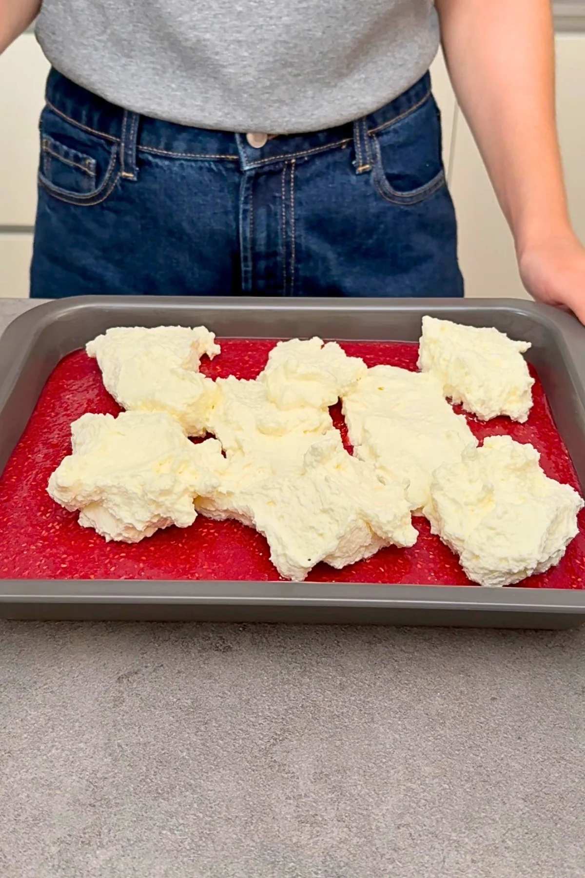 Steif geschlagene Sahnecreme wird in großen Portionen auf die gestockte Himbeerschicht gegeben