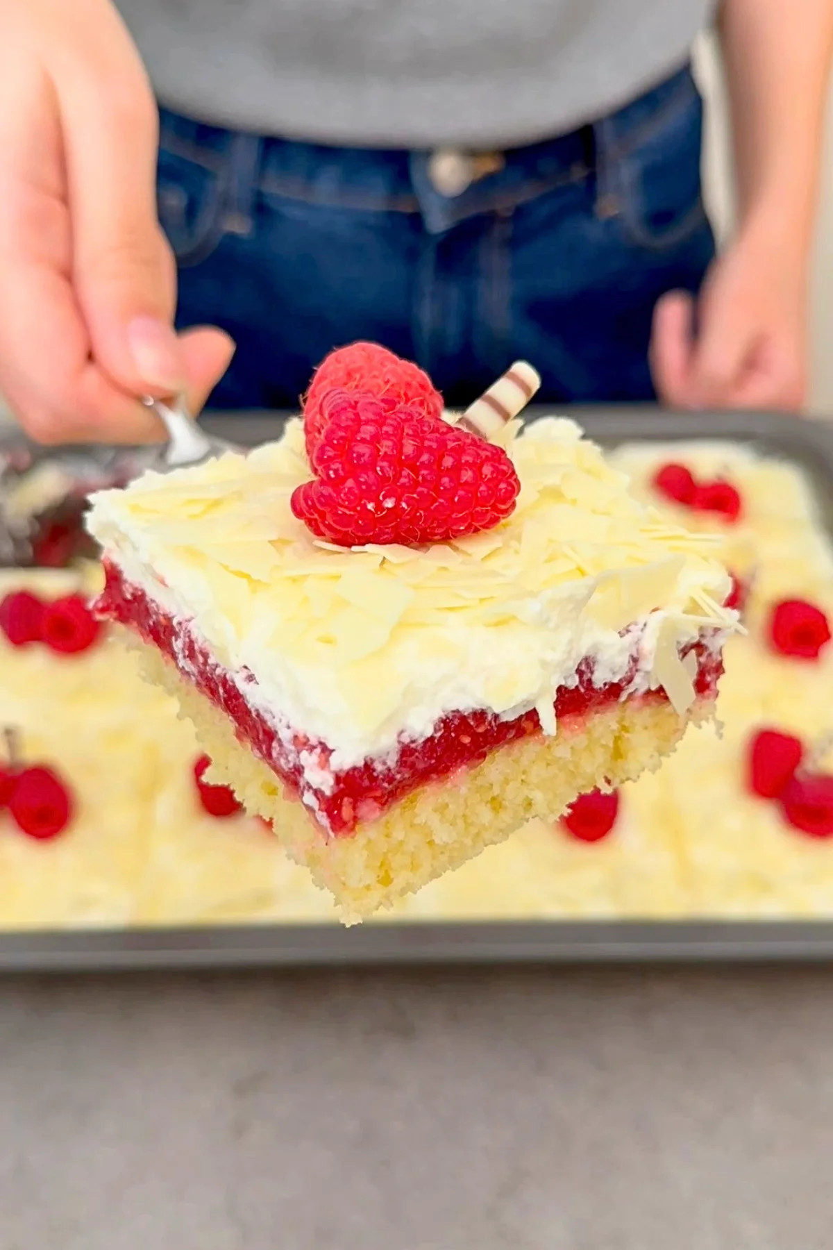 Stück Frau Holle Kuchen wird in die Kamera gehalten – saftige Schichten aus Biskuit, Himbeerfüllung und weißer Schokoladensahne