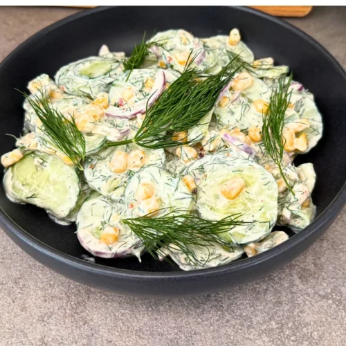 Gurke-Mais-Salat mit cremigem Joghurt-Dressing und frischem Dill in schwarzer Schüssel, Draufsicht