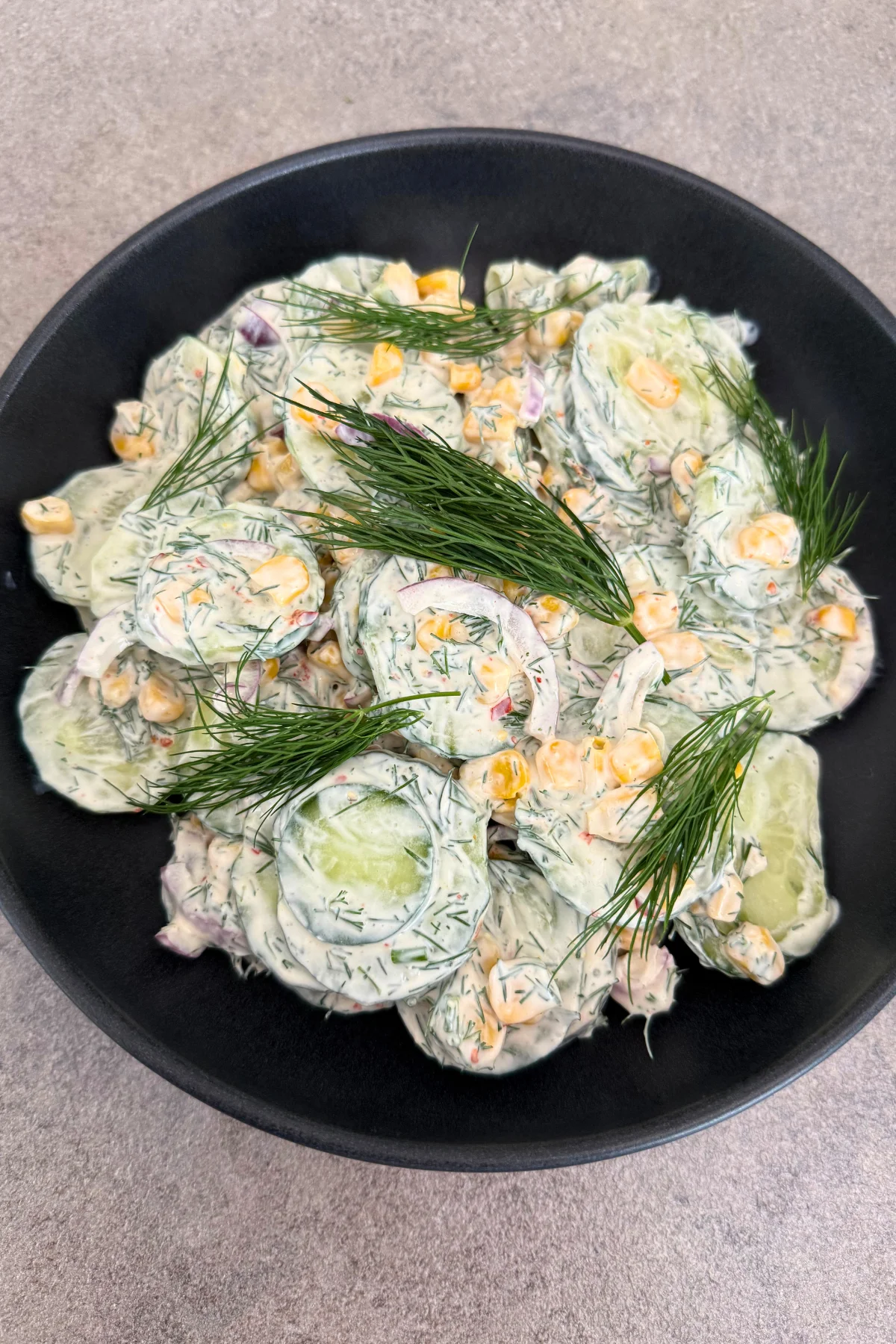 Fertig angerichteter Gurke-Mais-Salat mit frischem Dill in schwarzer Schüssel, Draufsicht hochformat