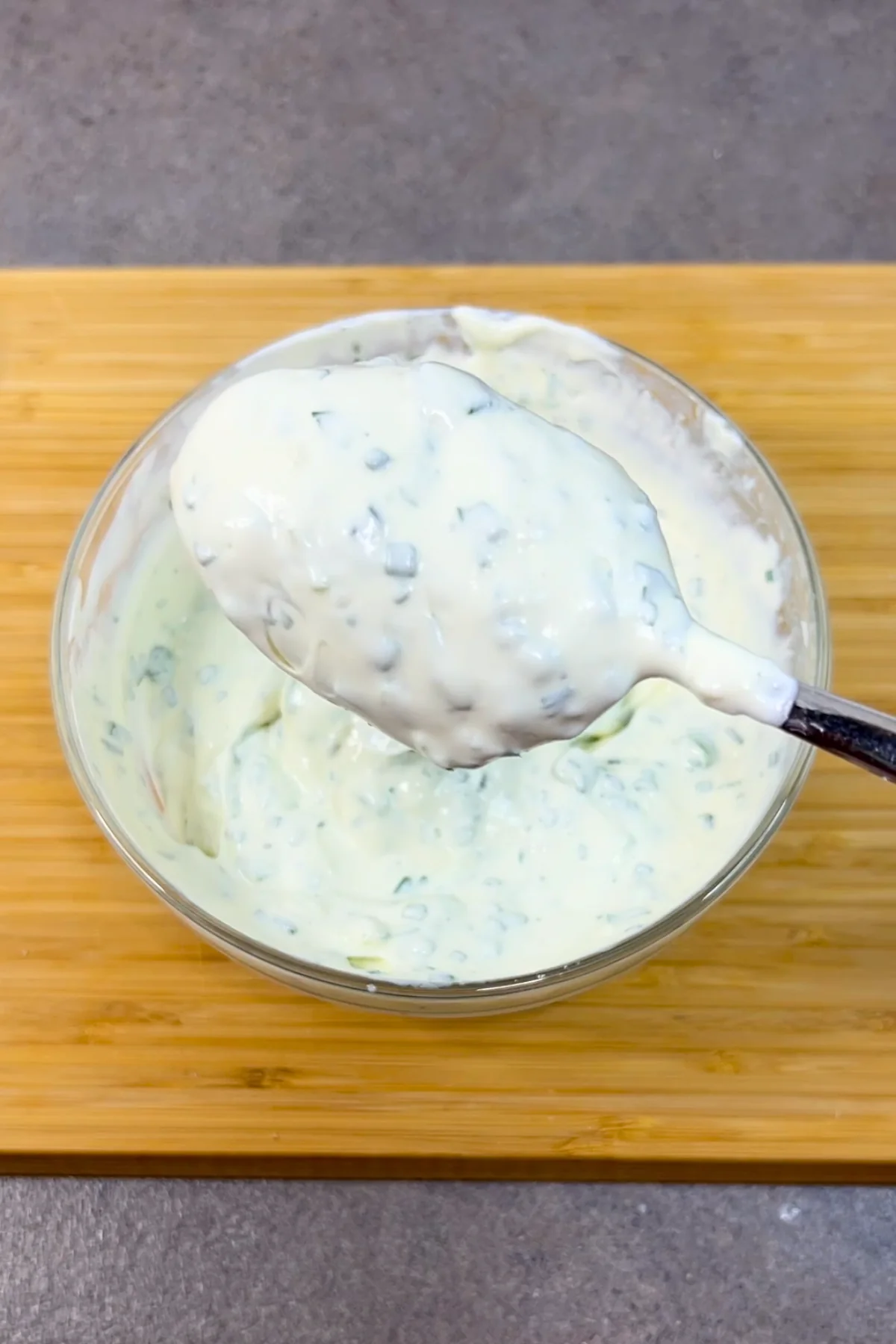 Fertiger Kräuterquark mit Frühlingszwiebeln wird mit dem Löffel aus der Glasschüssel gehoben