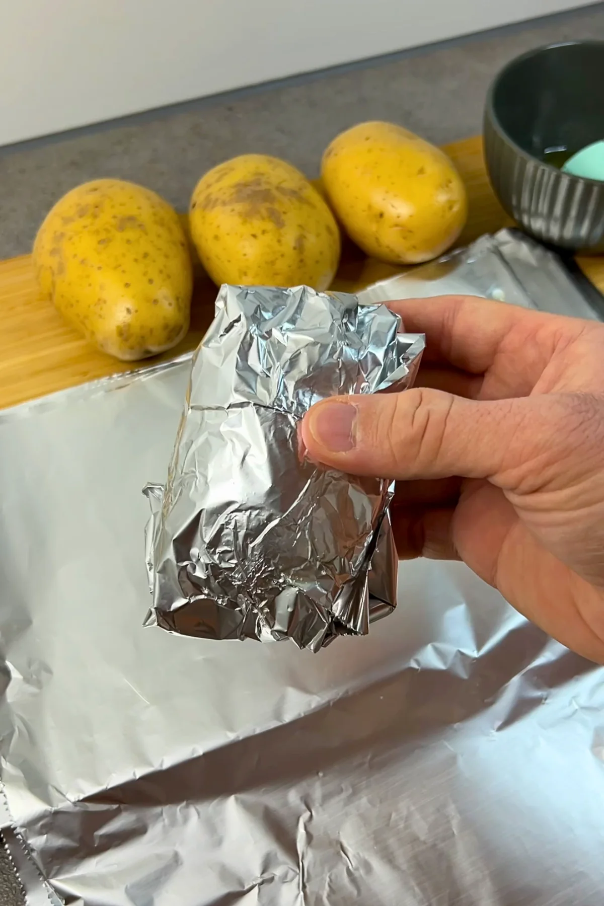 In Alufolie eingewickelte Kartoffel wird vor dem Backen in der Hand gehalten