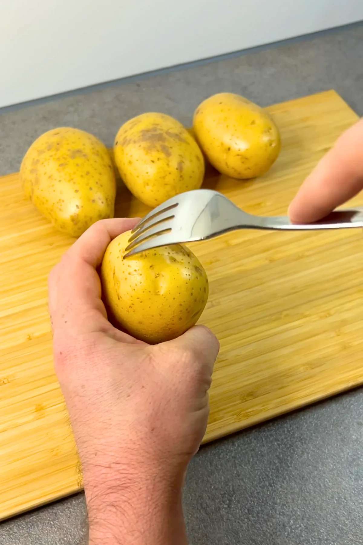 Rohe Kartoffel wird mit einer Gabel rundum eingestochen, drei weitere liegen auf dem Holzbrett