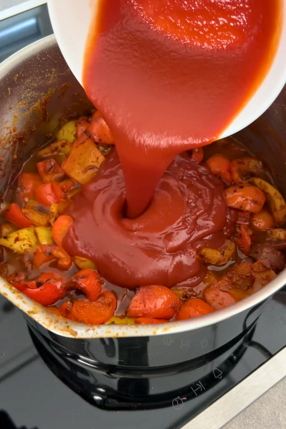 Tomatensoße wird aus einer weißen Schüssel in den Topf mit Paprika gegossen