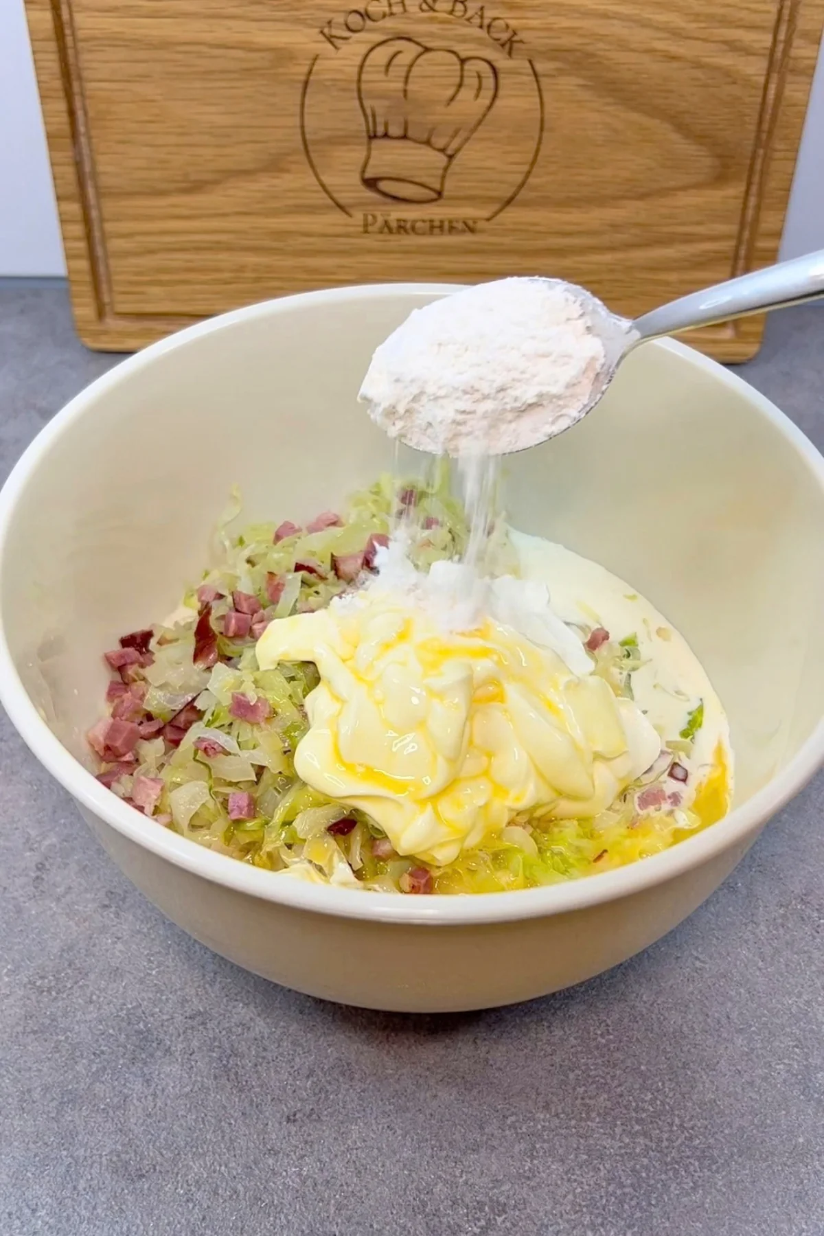 Ein Esslöffel Mehl wird zu Kraut, Speck, Sahne, Schmand und Ei in die Rührschüssel gegeben