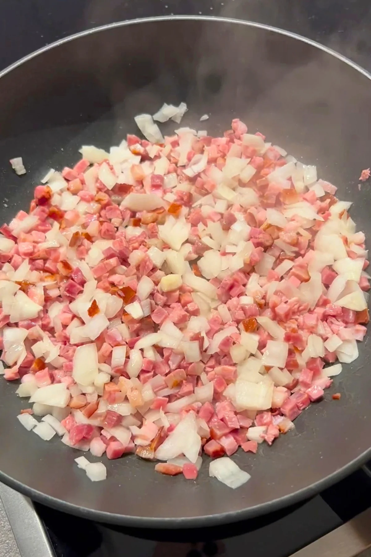 Rohe Speckwürfel und Zwiebelwürfel liegen ohne Öl in der beschichteten Pfanne