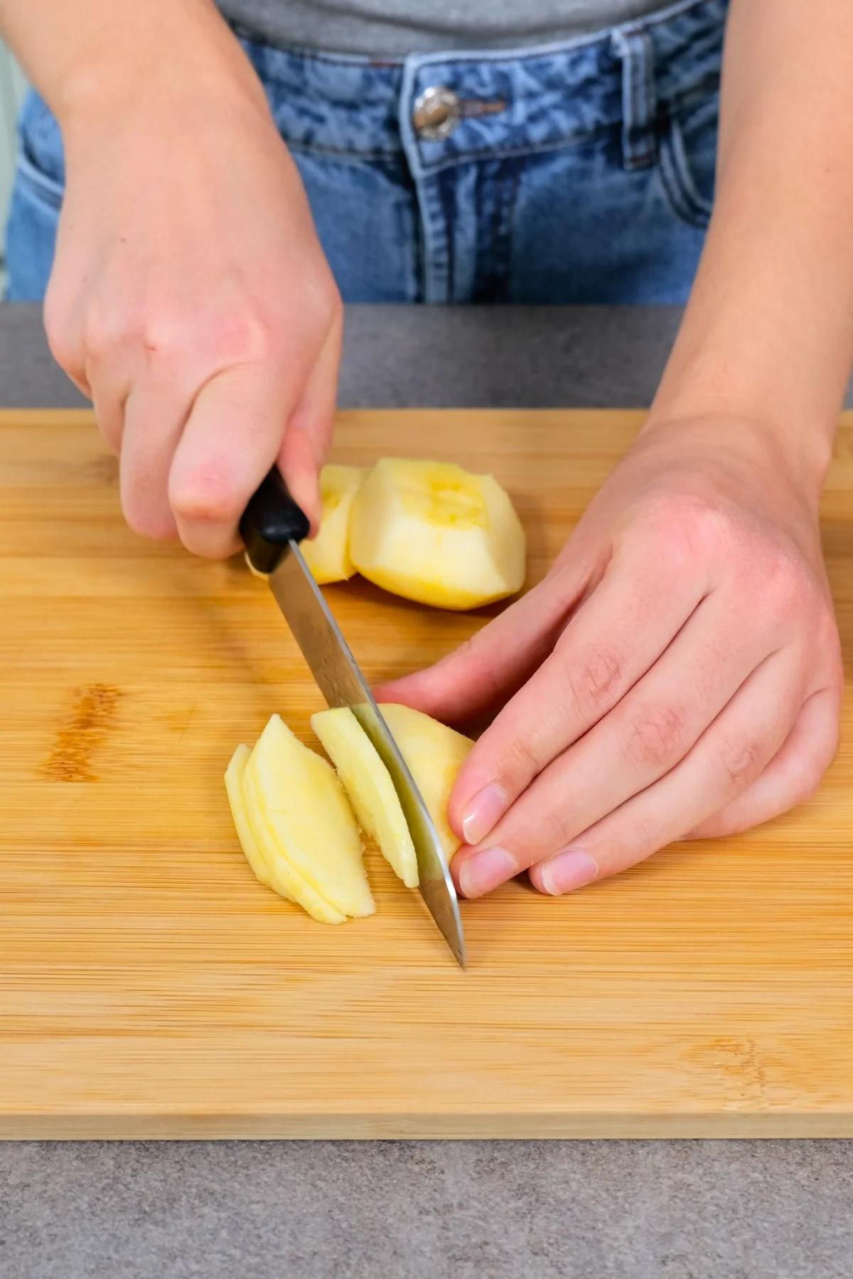 Ein geschälter Apfel wird auf einem Holzbrett mit dem Messer in dünne Scheiben geschnitten
