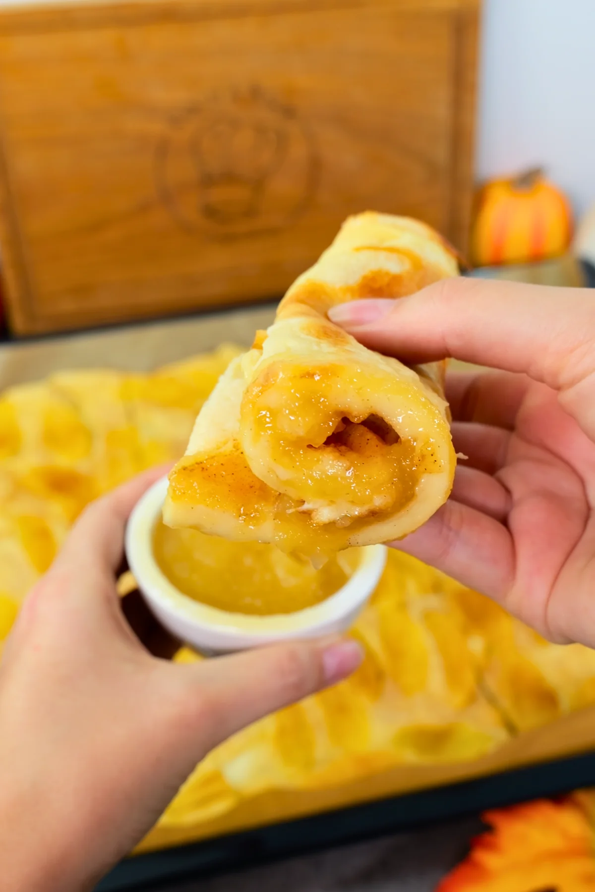 Eine Hand tunkt die aufgerollte Pfannkuchenbahn in ein weißes Schälchen mit Apfelmus