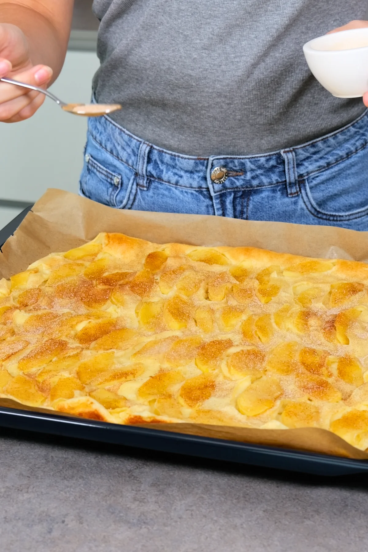 Zimtzucker wird mit einem Löffel über den fertig gebackenen Apfelpfannkuchen auf dem Blech gestreut