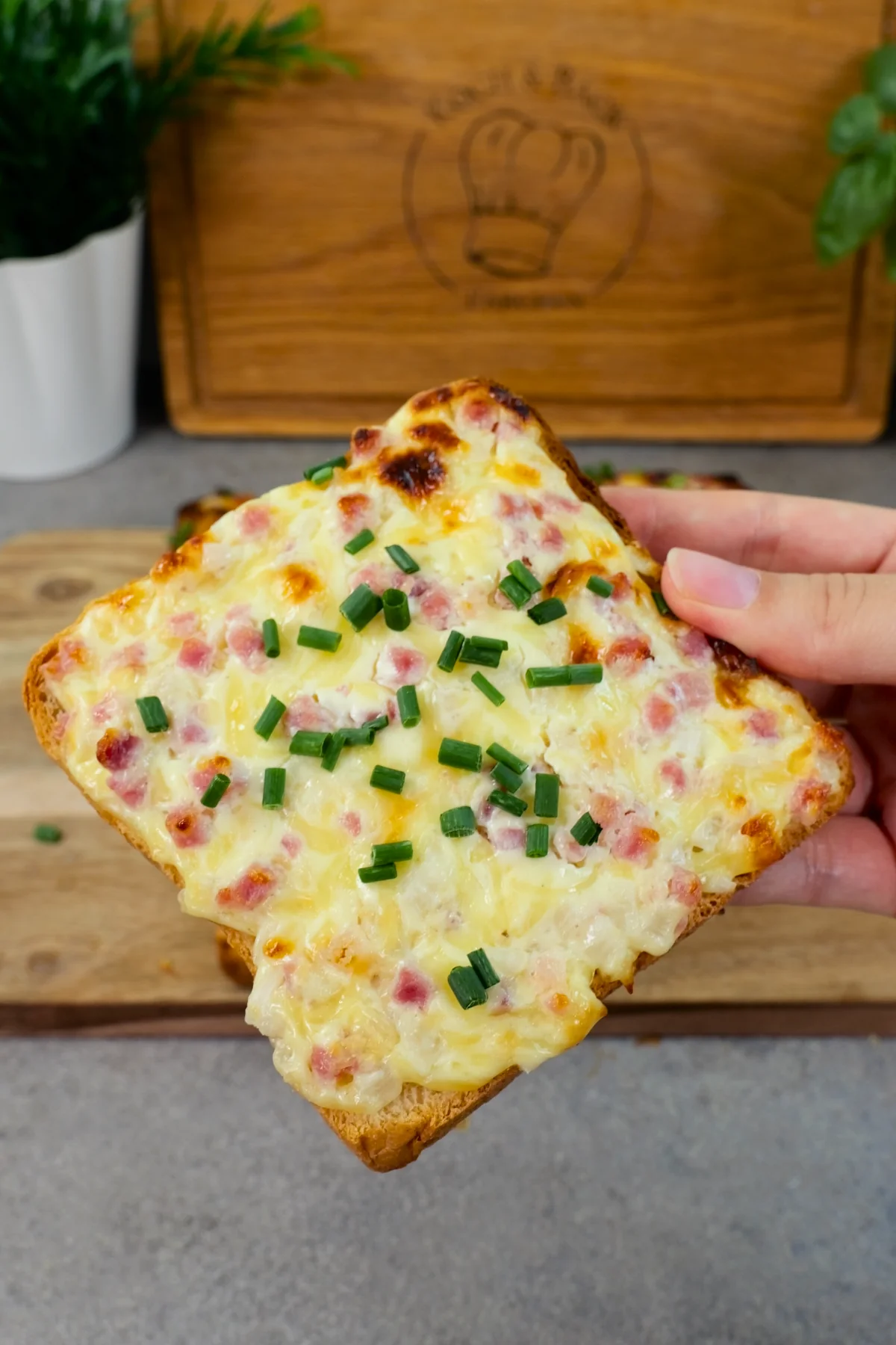 Nahaufnahme eines Flammkuchentoasts mit knusprigem Rand, braunen Käseflecken und Schnittlauch obenauf