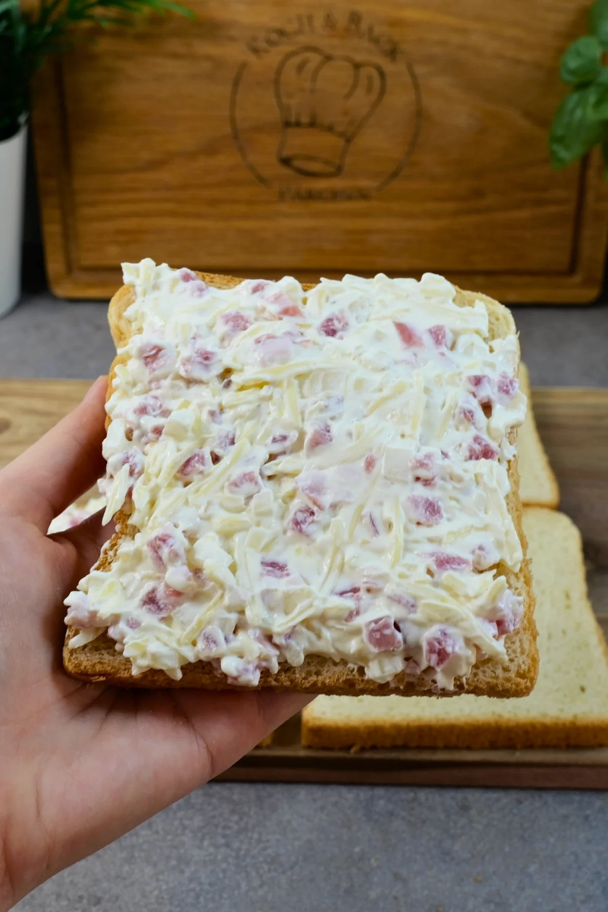 Eine Toastscheibe ist dick mit der Schmand-Käse-Masse bestrichen und wird über den übrigen Scheiben gehalten
