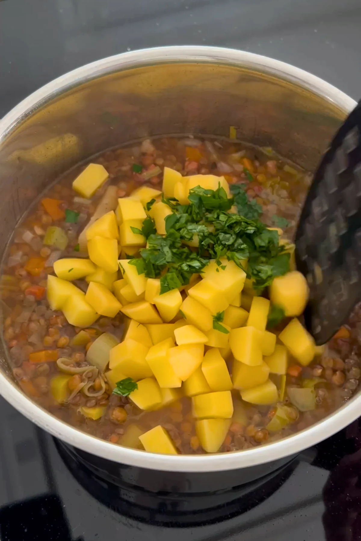 Rohe Kartoffelwürfel und gehackte Petersilie liegen auf den vorgegarten Linsen im Topf