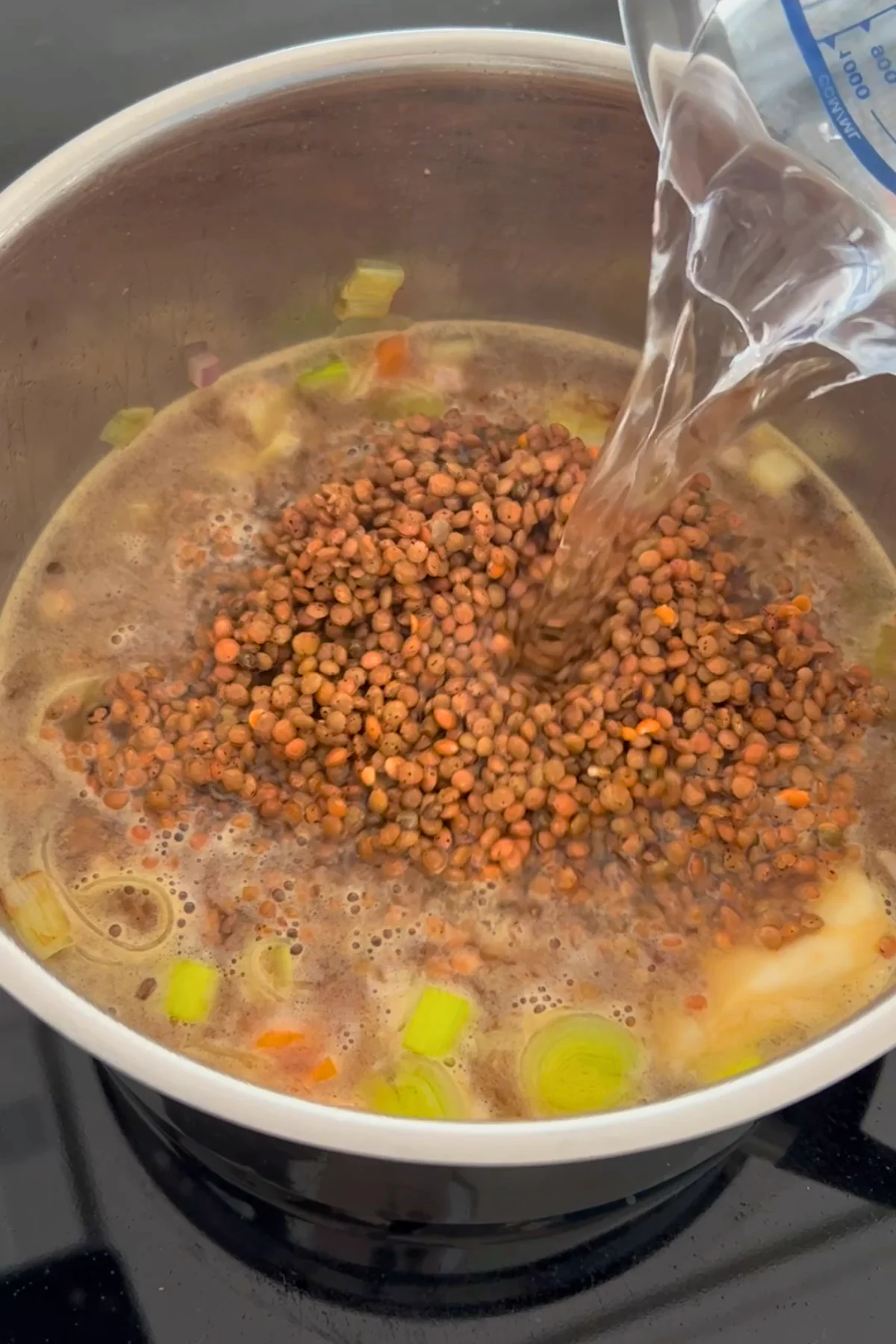 Berglinsen werden in den Topf gegeben, während gleichzeitig Wasser aus einem Messbecher dazugegossen wird