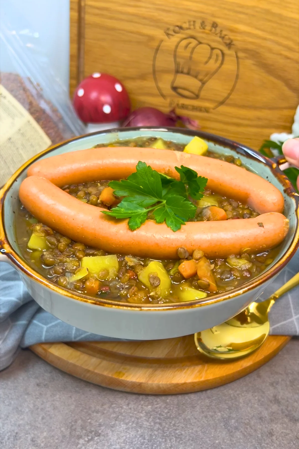 Blick von vorn in die Schale, Kartoffelwürfel und Karottenstücke liegen zwischen den Linsen unter den Würstchen