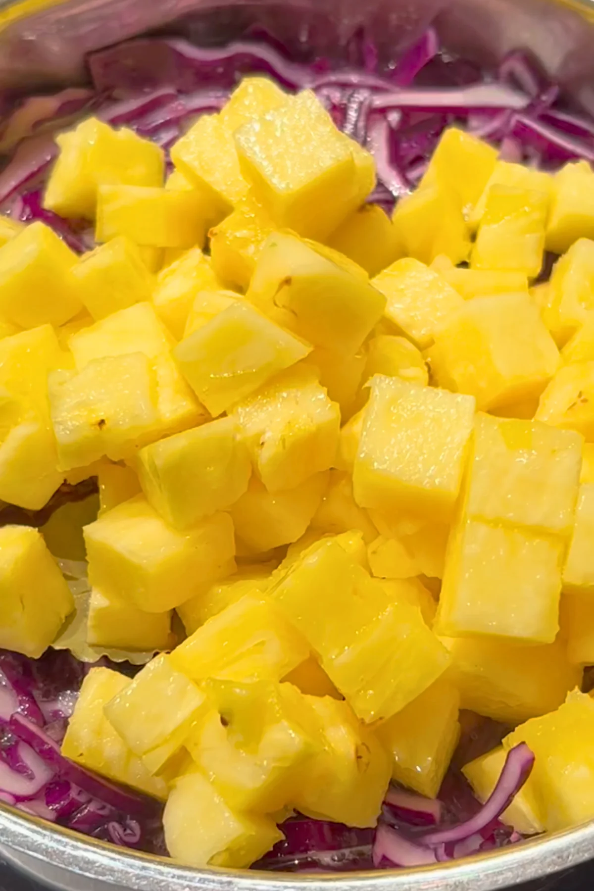 Gelbe Ananaswürfel liegen auf dem eingefallenen Rotkohl im Topf