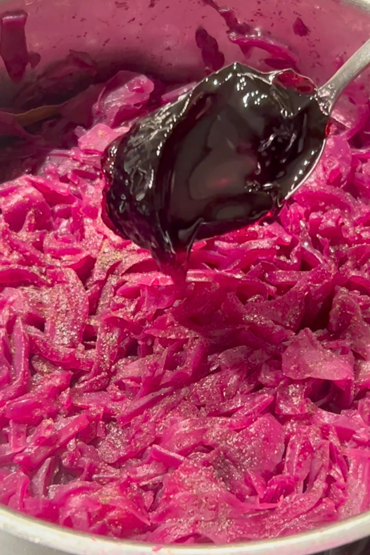 Dunkles Johannisbeergelee wird mit dem Löffel zum fertig geschmorten Rotkohl gegeben