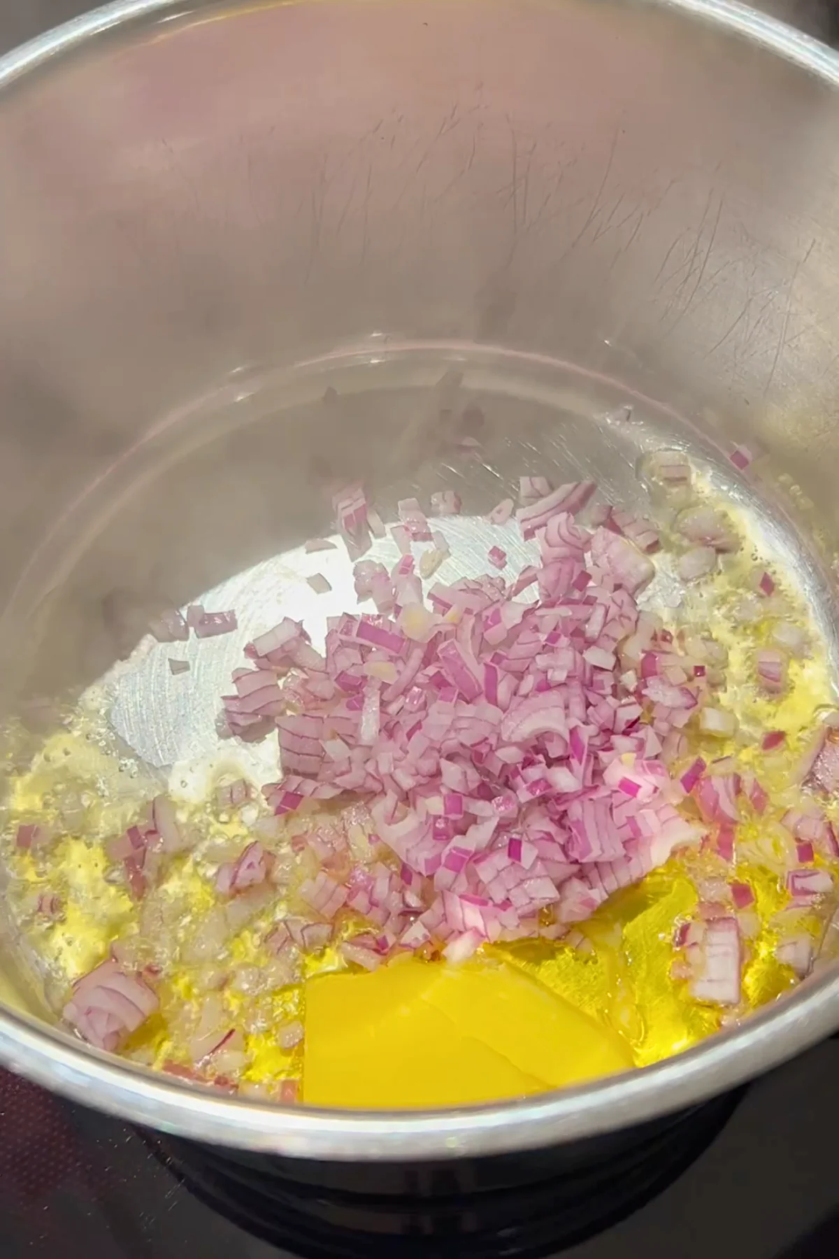 Fein gewürfelte Zwiebeln schwitzen in geschmolzenem Butterschmalz im Edelstahltopf an