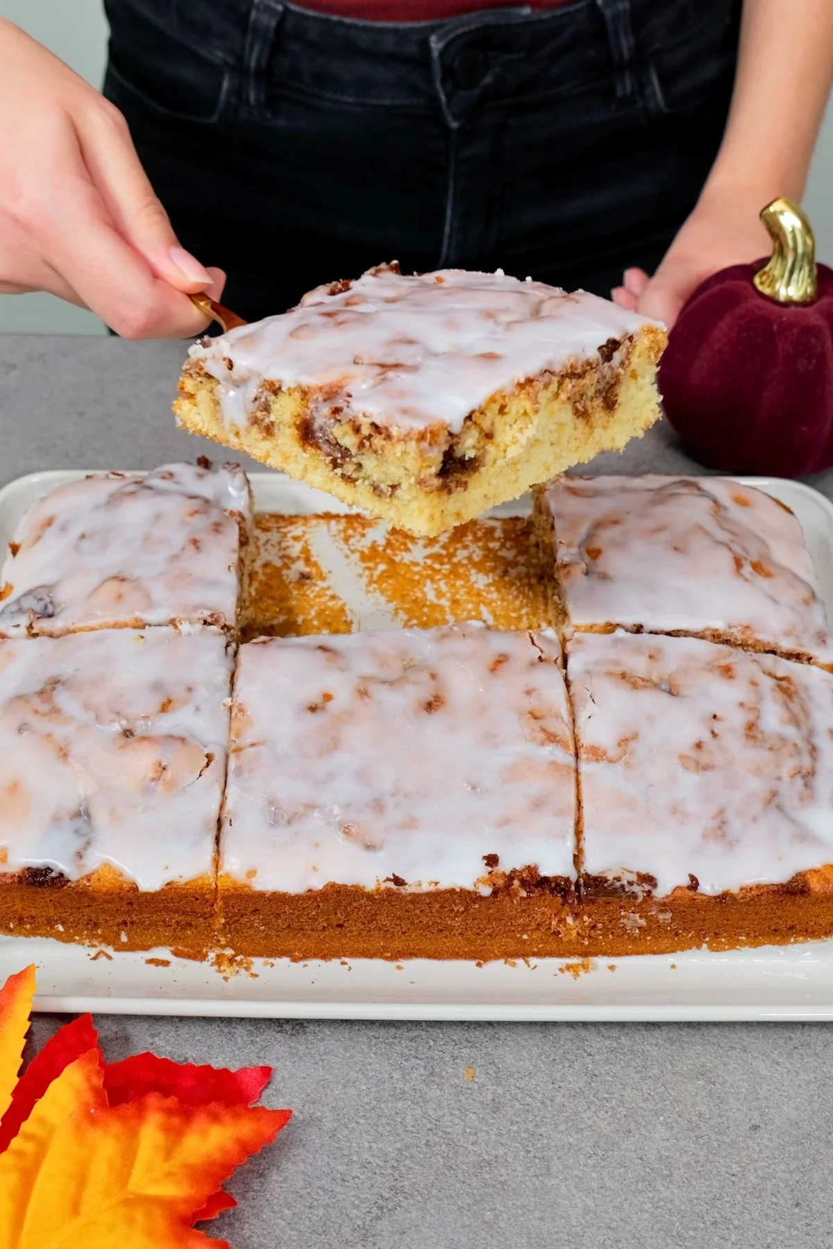 Ein Stück Zimtschneckenkuchen wird mit dem Kuchenheber vom Blech abgehoben, die Zimtspirale ist im Anschnitt zu sehen