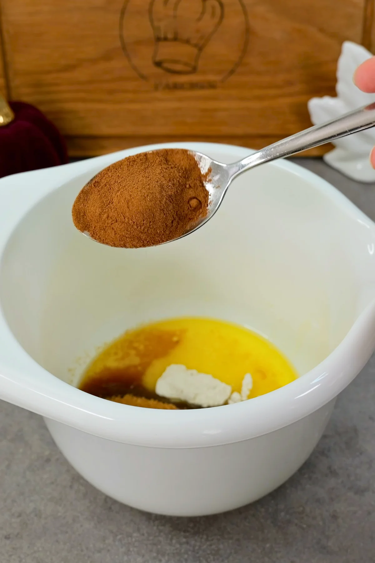 Ein gehäufter Löffel Zimt wird über die flüssige Butter mit braunem Zucker in der weißen Schüssel gehalten